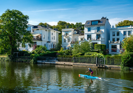 Water sports enthusiasts and excursion boats in the front of expensive luxury properties on the Alster in Hamburg Winterhudeのeditorial素材
