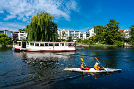 Water sports enthusiasts and excursion boats in the front of expensive luxury properties on the Alster in Hamburg Winterhudeのeditorial素材