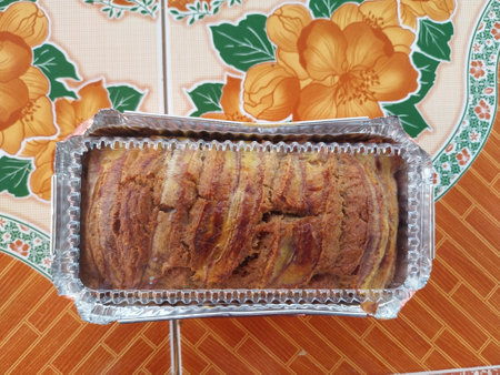 Banana cake in a foil box on a colorful tablecloth.