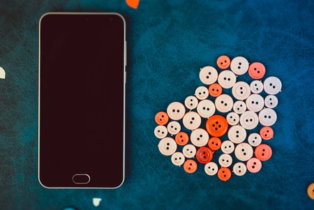 modern black smartphone with sewing buttons in the shape of a heart on a retro blue background