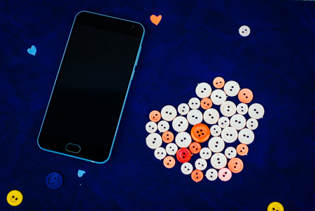 modern black smartphone with sewing buttons in the shape of a heart on a retro blue backgroundの写真素材
