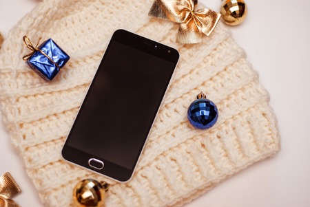 Smartphone and winter hat on white background. Black smart phone with black screen, with copy space and accessoriesの写真素材