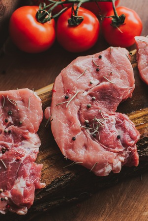 Pieces of raw pork steak with spices and herbs rosemary, thyme, basil, salt and pepper on a wooden background in rustic style, top viewの写真素材
