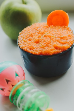 Baby food carrot puree with green apples in ceramic bowl on white backgroundの写真素材