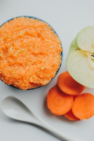 Baby food carrot puree with green apples in ceramic bowl on white backgroundの写真素材