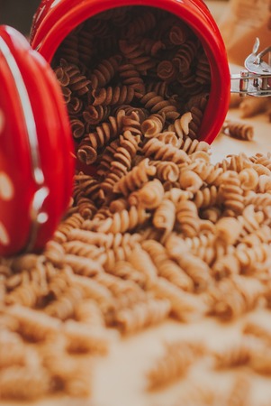 wholemeal pasta from organic spelt falling out of a red jar on a paper craftの写真素材