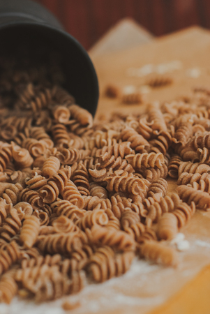 wholemeal pasta from organic spelt falling out of a black mug on a paper craftの写真素材
