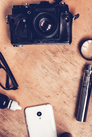Vaping set, vintage camera, smartphone and coffee on the wood table. Hipster or bussinesman style. Trendy objects with copy space on the wooden backgroundの写真素材