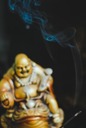 Burning incense sticks with laughing golden Buddha on the toadの写真素材