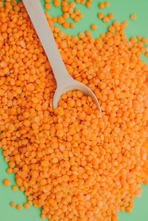 Red lentil in wooden spoon on green backgroundの写真素材