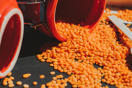 Red lentils in wooden spoon composition on black backgroundの写真素材