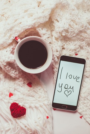 Hot coffee, smartphone, red heart on white knitted scarf