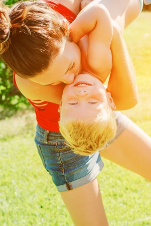 Young brunette mother lifting her son in park having fun enjoying motherhood.の写真素材