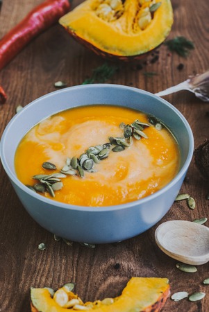 Roasted pumpkin and carrot soup with cream and pumpkin seeds on white wooden background.の写真素材