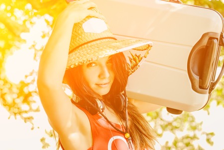funny young girl in a straw hat holding a big suitcase, going on a tripの写真素材