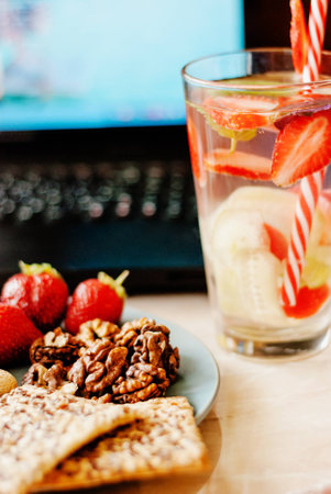 Office employee with laptop, healthy snack, water with strawberry and cucumber. Having strawberries, peanut, walnut, crispbread while working.の写真素材