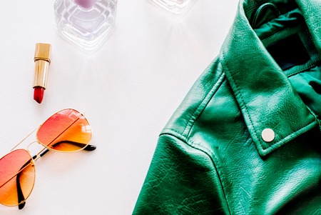 Green leather jacket and sunglasses on white background. Alternative fashion set. Flat lay, top...