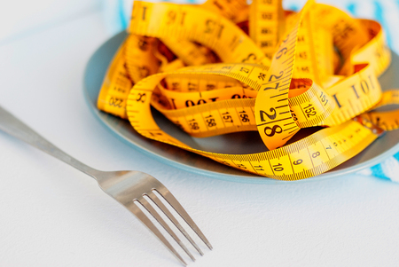 The concept of the diet. The fork rewound centimeter lying on plate closeupの写真素材