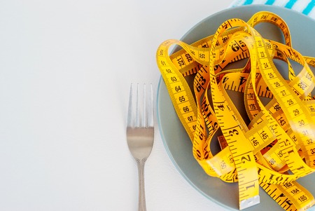 The concept of the diet. The fork rewound centimeter lying on plate closeupの写真素材