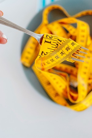 The concept of the diet. The fork rewound centimeter lying on plateの写真素材