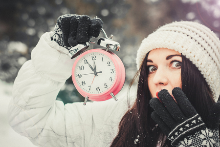 Woman in winter wear holding an alarm clockの写真素材