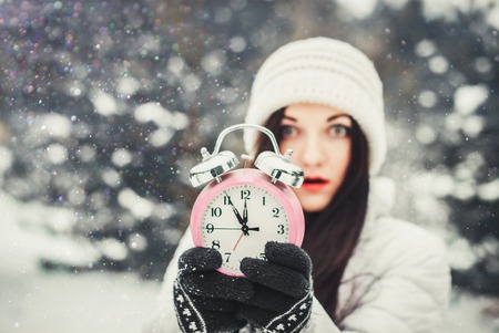 Woman in winter wear holding an alarm clockの写真素材