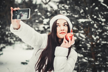 Girl taking selfie. Christmas girl outdoor self portrait. Woman in winter clothes and claus hat on a snow fieldの写真素材