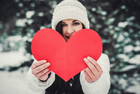 Beautiful young woman holding a red heart in the hands.