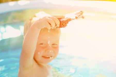 Baby with toy plane in swimming pool. Little boy learning to swim in outdoor pool. Swimming with kids. Healthy sport activity for children.の写真素材