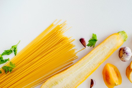 Italian food concept. Spaghetti with yellow zucchini, tomato ,garlic,champignon, parsley on white background flat lay and copy space.の写真素材