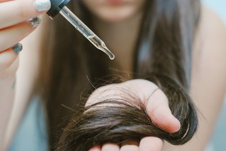 Young woman applying oil onto her hairの写真素材