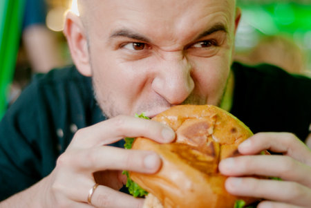 Man in a restaurant eating a hamburger, he is hungry and having a good bite. selective focusの写真素材