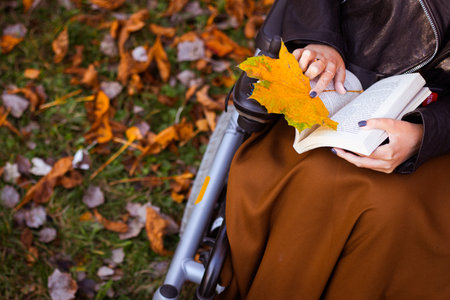 woman sitting on a wheelchair and reading a book while relaxing at a parkの写真素材