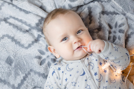 A baby boy lies on the bed and plays with a Christmas garland.. High quality photo