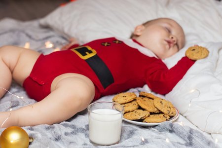 Cute child sleeping in Santa Claus costume beside standing milk and cookieの写真素材
