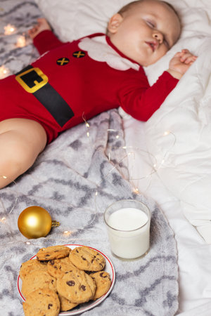 Cute child sleeping in Santa Claus costume beside standing milk and cookieの写真素材