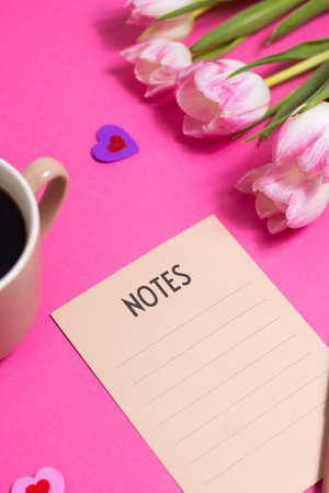 Notes with pen, cup of coffee, tulip spring flower and cute hearts on pink background, flat layの写真素材
