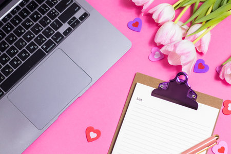Female workspace with laptop, tulips, accessories, notebook, cup of coffee on pink background
