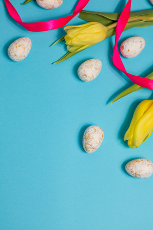 Yellow tulip flowers and easter eggs on blue background. Top view with copy space. Happy easter greeting cardの写真素材