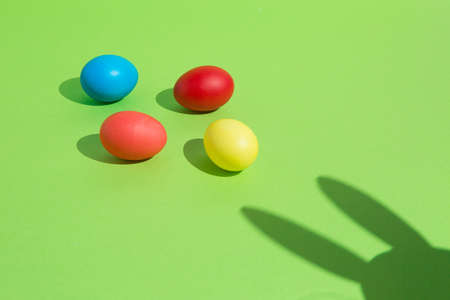 Colorful easter eggs with bunny shadow on vibrant green background. Minimal creative concept.