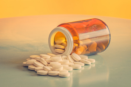 Pills and a glass on a table in orange lightの写真素材