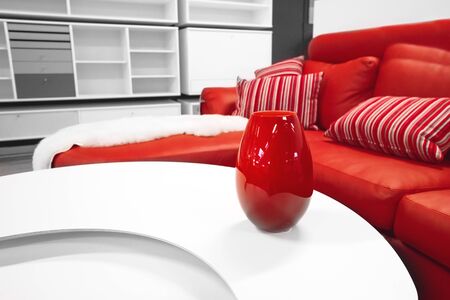 Red vase on a table in a stylish living room with a red couch with decorative pillows in white colorsの写真素材