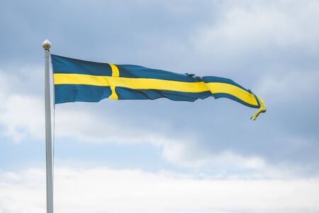 Swedish pennant flag on a flagpole in the wind in blue and yellow colors in cloudy weatherの写真素材