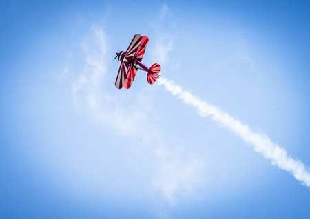 Red plane with propeller flying upward with white smoke on the tail in the blue skyの写真素材