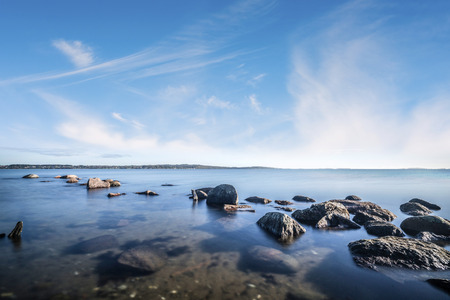 Rocks by the ocean in the calm water under a beautiful blue skyの写真素材