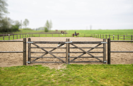 Wooden gate to an equine training course in a misty weather with green grass around the trackの写真素材