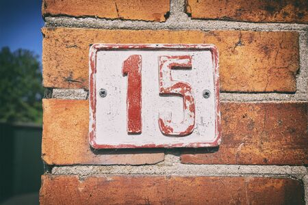 Street number 15 on a sign with pealing paint on a brick house in a streetの写真素材