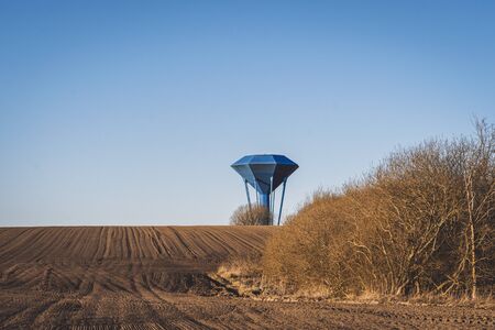 Blue water tower om a dry field with soil ready for the coming season