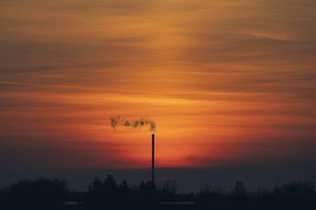 Smoke from a chimey in a beautiful sunset with industrial silhouettesの写真素材