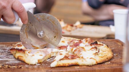 Homemade pizza being sliced on a wooden board in a kitchenの写真素材